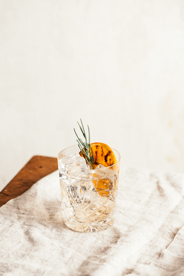 Ein elegantes Glas mit klarem Getränk, gefüllt mit Eiswürfeln, garniert mit einer Orangenscheibe und Rosmarin.